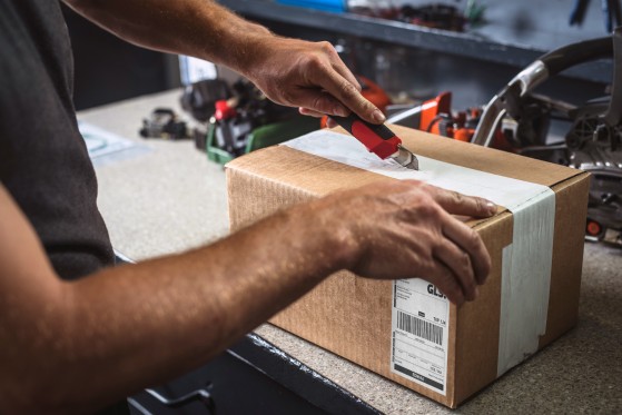 Hands opening a box using a box cuter in a workshop.
